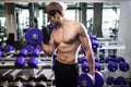 Athletic shirtless young male fitness model holds the dumbbell with light in gym Royalty Free Stock Photo