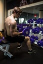 Athletic shirtless young male fitness model holds the dumbbell with light in gym Royalty Free Stock Photo