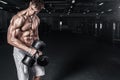 Athletic shirtless young sports man - fitness model holds the dumbbell in gym. Copy space fore your text. Royalty Free Stock Photo