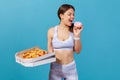 Athletic slim woman in white sportswear losing willpower and biting sweet junk donut, making choice holding in hand pizza box,