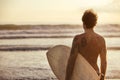 Athletic surfer stands with surfboard at sunset beach Royalty Free Stock Photo