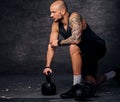 Sporty shaved head sporty male standing in knee and holds Kettlebell.