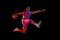 Athletic teen boy training, playing basketball against black studio background in neon light. Competitive spirit