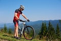 Athletic tourist biker looking at his bike on mountain hill on bright blue summer sky Royalty Free Stock Photo