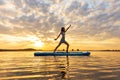 athletic woman doing YOGA on a inflatable SUP board on through shining water surface