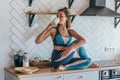 Athletic woman having breakfast in the kitchen, girl sitting on table and drinking