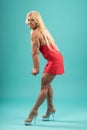 Athletic woman in red dress posing in studio. Attractive fitness lady with long blond hair showing her muscles. Royalty Free Stock Photo