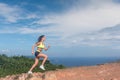 Athletic woman running up the mountain with sky and sea in background. Professional runner doing cardio work-out outdoor