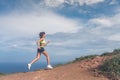 Athletic woman running up the mountain with sky and sea in background. Professional runner doing cardio work-out outdoor