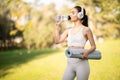 An athletic woman in stylish sportswear hydrates while drinking from a water bottle