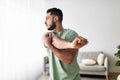 Athletic young Arab guy stretching arm muscles, doing warmup exercises at home, selective focus Royalty Free Stock Photo