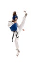 Athletic young girl in dobok and blue helmet practicing, training taekwondo isolated over white background