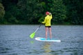 Athletic young girl-surfer riding on the stand-up paddle board in the clear waters of the on the background of green trees Royalty Free Stock Photo