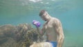 Sportsman is training with dumbbells underwater, making hand exercises near the coral reefs with fish.