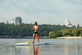 Athletic young man with a naked torso floats on the river on a sup board, rowing with an oar on the background of a beautiful