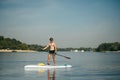 Athletic young man paddles standing on a sup board on the river and looks to the side. A muscular man is active on the water