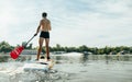 Athletic young man swims along the river on a paddle board, view from the back. Athlete trains on a sup board, actively paddles