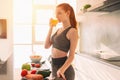 Athletic young red haired woman in the kitchen drinks a glass of fruit centrifuged juice