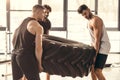 athletic young sportsmen lifting tyre together