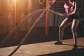 Woman working out in training gym doing cross fit exercise with battle ropes