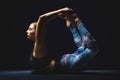 Athletic young woman doing yoga. Black background, charming light, serene mood.