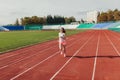 Athletic young woman in sportswear sprinting on running track stadium at sunset