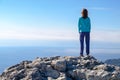 Athletic young woman standing on the rocky top of the mountain against the blue of sky and sea