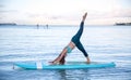 Athletic young woman in SUP Yoga practice side bend leg lift Pose in Ala Moana Hawaii