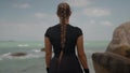 Athletically built female standing on the big stone by the ocean and looks ahead