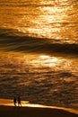 Atlantic ocean in golden morning sunlight reflections with silhouette of two people walking on Copacabana beach, Rio de Janeiro, B Royalty Free Stock Photo