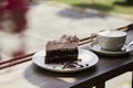 Atmosperic natural piece of cake and a glass of cappuccino on wooden table outdoor in the cafe terrace. Aesthetic coffee