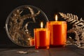 Atmosphere burning orange candles in orange glass with dry leaves, round mirror as elegant home decor