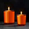 Atmosphere burning orange candles in orange glass as elegant home decor on black wood table in darkness