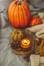 Atmospheric candles - shape of pumpkins and candle in amber glass jar and autumn decor on gray bed. Autumn cozy home and hygge