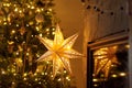 Atmospheric christmas eve. Stylish christmas illuminated star, decorated christmas tree with golden lights and festive decor on