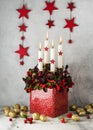 Atmospheric Christmas floral decoration. Red checkerberry plant with four white burning candles and wooden stars in a tin pot.