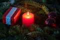 Christmas motif with red burning candle surrounded by Nordmann fir branches, red christmas tree balls and gift parcel Royalty Free Stock Photo