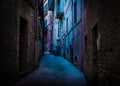 A dark and narrow, back alley painted with blue and magenta light taken in Recanati, Macerata, Italy
