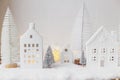 Atmospheric miniature white christmas village. Stylish little christmas houses and trees on snow blanket with glowing lights. Royalty Free Stock Photo