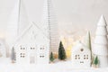 Atmospheric miniature white christmas village. Stylish little christmas houses and trees on snow blanket with glowing lights. Royalty Free Stock Photo