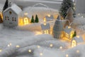 Atmospheric miniature winter village. Stylish little ceramic houses and christmas wooden trees on snow blanket with glowing lights Royalty Free Stock Photo