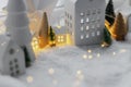 Atmospheric miniature winter village. Stylish little ceramic houses and christmas wooden trees on snow blanket with glowing lights Royalty Free Stock Photo