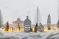 Atmospheric miniature winter village. Stylish little ceramic houses and christmas wooden trees on snow blanket with glowing lights Royalty Free Stock Photo