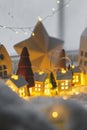 Atmospheric miniature winter village. Stylish little ceramic houses and christmas wooden trees on snow blanket with glowing lights Royalty Free Stock Photo