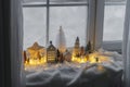 Atmospheric miniature winter village. Stylish little ceramic houses and christmas wooden trees on snow blanket with glowing lights Royalty Free Stock Photo