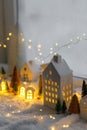 Atmospheric miniature winter village. Stylish little ceramic houses and christmas wooden trees on snow blanket with glowing lights Royalty Free Stock Photo