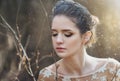 Atmospheric outdoor portrait of sensual young woman wearing elegant dress in a coniferous forest with rays of sunlight.