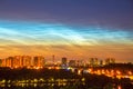 Atmospheric phenomenon glowing of noctilucent clouds. Night sky and spectacular silvery clouds, silhouettes of city buildings