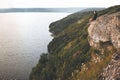 Atmospheric tranquil moment. Hipster traveler sitting on top of rock mountain and enjoying amazing view on river. Young guy Royalty Free Stock Photo