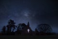 An atmospheric concept edit of a church with a glowing cross below a starry sky at night